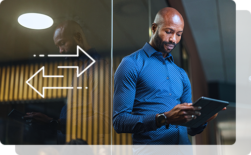 A young professional man stands in front of a glass office window, focused on a tablet, representing innovation and expertise in healthcare solutions.